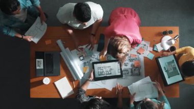 Yetenekli iş adamlarının tablet tutması ve planlara bakması. Masada dizüstü bilgisayarla dururken mimarın tasarım ve planlama bölümünün havadan görüntüsü. Sempozyum.