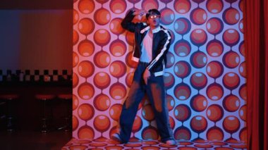 Asyalı break dansçı serbest stile geçiyor ve balon arka planlı kameraya bakıyor. Profesyonel hippi gündelik kıyafet giyer ve gözlük takar. Mutluluk.