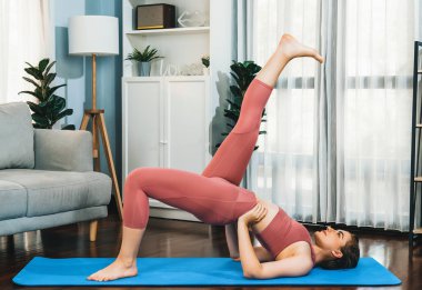 Spor kıyafetleri içinde esnek ve becerikli bir kadın evde egzersiz paspası üzerinde meditasyon pozisyonunda yoga yapıyor. Huzurlu ve huzurlu bir yoga yaşam tarzı..