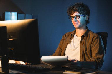 Genç işadamı, Neon Light Modern Ofis 'teki yeni proje surround çalışma masası için kağıt üzerinde tasarım düşünüyor. E-posta ile hediye göndermeden önce not defterine yeni bir iş düşünüyorum. Toplayıcı.