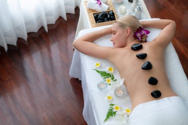 Lüks tatil beldesindeki kaplıca salonunda sıcak taş masajı. Gündüz huzurlu ortam, mutlu kadın müşteri bazalt taşı masajının keyfini çıkarıyor. Sessiz.