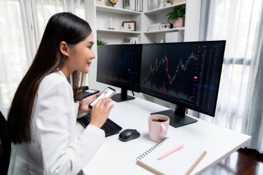 Mutlu yüzlü gülümseyen Asyalı genç iş kadını modern ofisteki döviz borsasının karlı grafiğinde akıllı telefonuyla karşılaştırıyor ve yüksek kâr amaçlı servet güvenliği sağlıyor. Taktik.