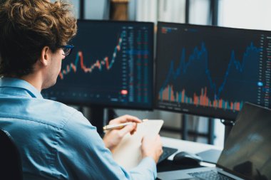 Piyasa stoku grafiği üzerinde çalışan genç profesyonel tüccar ev ofisindeki gerçek zamanlı ekranlara yatırım yaparak önemli döviz kuru kavramları yazarak analiz ediyor. Toplayıcı.