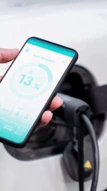 Akıllı telefon ekranı akıllı EV mobil uygulama üzerinde pil durumu EV araba garajdaki ev şarj istasyonu ile elektrik şarj ederken. Geleceğin yenilikçi EV arabası ve enerji sürdürülebilirliği. İnceleyin