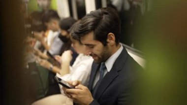 Gülümseyen beyaz iş adamı cep telefonuna bakıyor ya da trende otururken sosyal medya oynuyor. Çekici proje yöneticisi yoğun saatlerde toplu taşıma araçlarını kullanarak iş yerine gidiyor. Sevinçli..