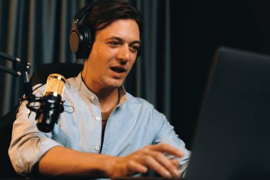 Sunucu kanalı akıllı yayıncı laptopta canlı sosyal medya uygulaması arıyor, kulaklık takıyor ve modern ofis stüdyosundaki mikrofonu kullanıyor. Bireysel.