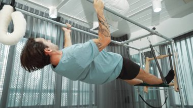 Çekirdek dayanıklılığı ve spor salonunda vücut egzersizi için pilates trapez masasına tırmanan bir adam. Eğitmen, arka ve kalça esnekliğini arttırmak için Cadillac 'ta ters asılı duruyor. Alışkanlık.