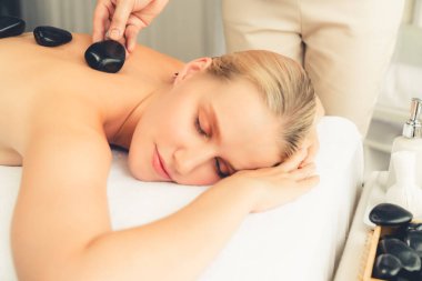 Lüks tatil köyündeki kaplıcalarda sıcak taş masajı. Gün ışığı sükunet ortamında, mutlu kadın müşteri bazalt taş masajından zevk alıyor. Rahatlatıcı bir sıcaklıkla vücudun üzerinde süzülüyor. Sessiz.