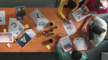 Toplantıda tasarımcı yazma ve logo grafiği tasarlamanın en üst görünümü. Renkli paletler üzerinde çalışan iş adamlarının yakınlaşması ve masaya kağıt ve ekipman ile yapışkan notlar yazmak. Sempozyum.