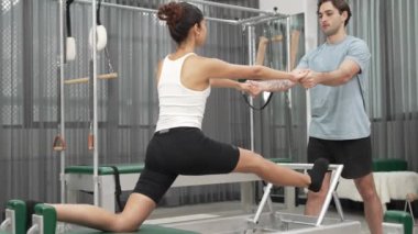 Esneklik ve çekirdek eğitimi için pilates kursunda trapez masasında destek alan bir kadın. Öğrenci dengeyi geliştirmek için reformcuları iki büklüm ediyor. Alışkanlık.