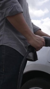 İlerici adam elektrik istasyonundan elektrik arabasına elektrik kablosu bağlıyor. Yeşil enerjiyle çalışan EV arabası gelecekteki temiz çevre konsepti için yeşil alanda çalışıyor..
