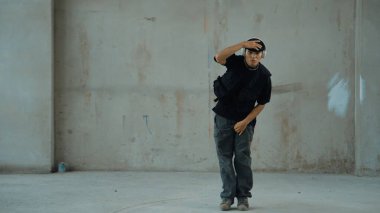 Kulaklıktan çimento arka planda müzik dinlerken break dans pratiği yapan yakışıklı bir hippi. Sokak dansçısının hareketli çekimi robot dansı yapar. Açık hava sporu 2024. Modern dans. hiphop.