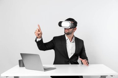 Profesyonel proje yöneticisi dizüstü bilgisayar başında otururken VR gözlüğü kullanıyor. Görsel gerçeklik kulaklığı takan yetenekli bir iş adamı metaevren ya da görsel dünyayı birbirine bağlıyor. Yenilik. Sapma.