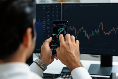 Akıllı telefondan akıllı telefon arayan tüccar işadamı, bilgisayardaki dinamik borsa yatırım ekranını analiz ediyor ve modern merkez ofisteki en kârlı finansal teknoloji pazarına yatırım yapıyor. Tahmin et..