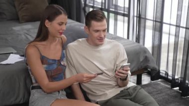 Genç çift, kredi kartıyla ödemek için internet üzerinden ödeme uygulaması ve dijital cüzdan kullanarak yatak odasında oturuyor. Mobil internet üzerinden alışveriş ve modern alımlar. Düzenle
