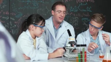 Zeki öğretmen, çeşitli öğrencilerin yaratıcı eğitim üzerine yazılmış bilim teorisiyle karatahta önünde deney yaparken test tüpü masanın üzerine yerleştirilirken mikroskop altında bakar.