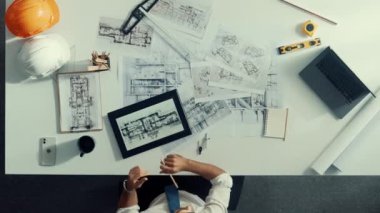 İnşaat mühendisi inşaatı planlarken ve proje planı ve dizüstü bilgisayarla toplantı masasında otururken planlara bakarken tepeden tırnağa. Mimar bina tasarımı hakkında not alıyor. Hizalama.
