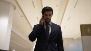 Profesyonel bir iş adamı yürüyen merdiven kullanırken telefonla konuşuyor. Beyaz tenli yönetici, pazarlama fikri ya da planı rapor etmek ve tartışmak için iş ekibiyle konuşuyor. Ön manzara. Sevinçli..