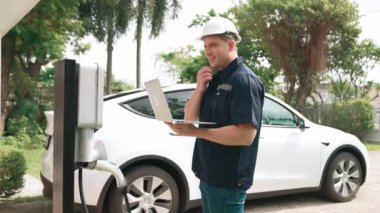 Evde EV şarj istasyonu kurulumu üzerinde çalışan nitelikli teknisyen, EV için dizüstü bilgisayarla şarj sisteminde sorun çıkarma ve yapılandırma ayarları yapıyor. Titiz