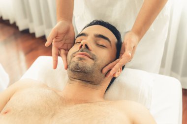 Beyaz adam stres önleyici kafa masajından ve lüks bir tatil beldesi veya otel spa salonundaki modern ışık ortamında yüz güzelliği eğlencelerini şımartmaktan hoşlanıyor. Sessiz.