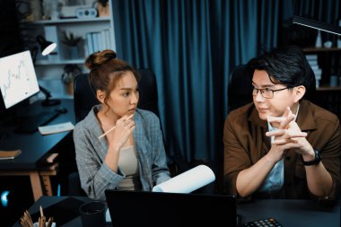 Stresli suratlı iki yönetici birlikte evrak işlerini tartışıyorlar. Modern ofiste gece geç saatlerde dizüstü bilgisayarla karşılaştırıldığında şirket projesinde çalışıyorlar. İnfobahn.