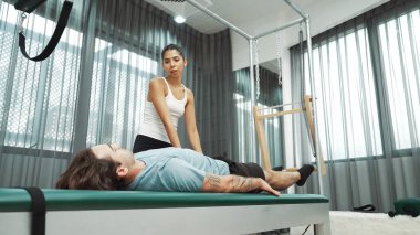 Cadillac ekipmanları üzerinde bacak kaldırma egzersizinde müşteriye yardımcı olan yetenekli pilates eğitmeni. Kadın antrenör, Cadillac 'ın bacak gerdirme hareketine yardım ediyor. Temel bağlantıyı geliştirmek için, bacak esnekliği için. Alışkanlık.