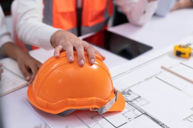 Mimari proje üzerinde birlikte çalışan çeşitli inşaat mühendisi ve müvekkil grupları, inşaat planını gözden geçirip toplantı masasında plan oluşturuyorlar. Tedbirli