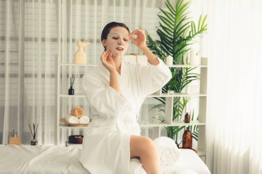 Kaplıca salonunun sakin, modern gün ışığı atmosferi, kadın müşteri poz veriyor ve yüz maskesi ile gençleştiriyor. Yüz bakımı ve güzellik kozmetolojisi prosedürü. Sessiz.