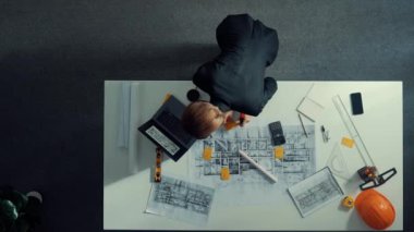 Yetenekli proje yöneticisinin proje planının üst görüntüsü ve toplantı masasında ekipman, cetvel, güvenlik miğferi ve dizüstü bilgisayarı olan mimar mühendise ev tasarımını açıkla. Hizalama.