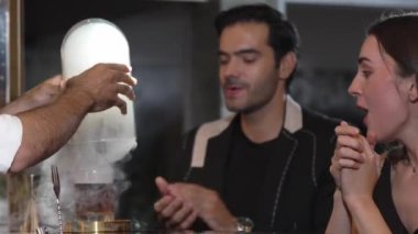 Duman çıkaran dumanlı bir barmen kokteyl sunumuyla viskiyi karıştırıyor. Grup misafirlerine içki tezgahında özel hoş geldin içkisi öneriyor. Vinosity.