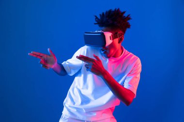 VR kullanan genç Afrikalı Amerikalı oyuncu sanal gerçeklik dünyasını dijital fütüristik teknolojiye bağlayan mavi neon ışıklandırma duvarında 3 boyutlu sanal silah avcısını kullanıyor. Entrika.