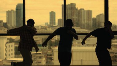 Yetenekli koreograf grubunun gökyüzü dövüşçüsüyle dans ederken çekilmiş siluet fotoğrafı, şehir manzarası arka planı. Genç hipster takımı dans gösterisi. Sarı filtre. Gölge. Açık hava sporu 2024 hiphop..