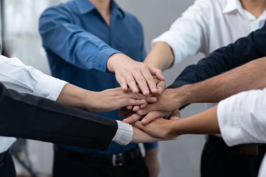 Çeşitli ofis çalışanlarından oluşan bir grup, ofis odasında el ele vererek iş sinerjisini ve iş yerindeki güçlü verimli takım çalışmasını sembolize ediyor. İş çalışanları arasındaki işbirliği ve birlik. Tedbirli