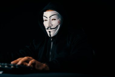 Kameraya bakan beyaz sırıtan isimsiz suçlu maskesi ana veritabanı sunucu sistemi aracılığıyla bilgisayar fidye şirketinin gizliliğinde başarıyla hacklenen virüs şifrelemesi yüklüyor. Tahmin et..