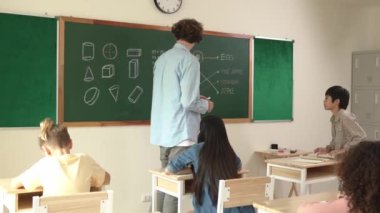 Asyalı çocuk cevap yazmayı bitirirken öğretmen de çocuğu teşvik etmek için el çırpıyor. Öğretmen matematik dersinde öğrenciyi alkışlarken ve el çırparken çekici öğrenci koltuğuna geri dönüyor. Pedagoji.