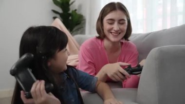 Çekici kız oyun oynayıp otururken anne kanepeye uzanıp beşlik çakıyor. Beyaz bir ebeveyn ve çekici bir kız, elinde joystick ile birlikte vakit geçirir ve maç kazanmaya odaklanırlar. Pedagoji.