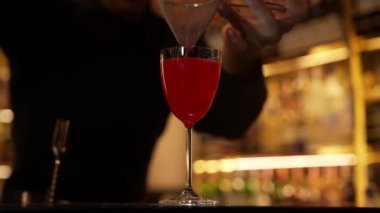 Yakından el barmeni, lüks tezgahta kırmızı kokteylde süzgeç karışık votka kullanıyor. Hazırlık, Bokeh Light 'taki bar ve restoranda gece kulübü temalı özel içecekler hazırlıyor. Vinosity.