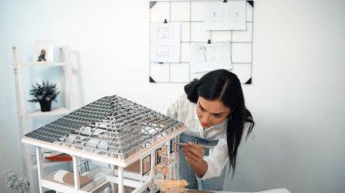 Young beautiful caucasian architect engineer turns house model around to inspect house construction and check mistake point to solve the problem on meeting table at modern office. Closeup. Immaculate. clipart