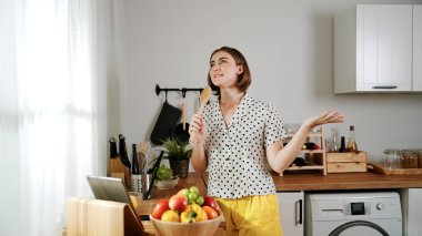 Enerjik beyaz anne kahvaltı için salata pişirirken ve yemek pişirirken elinde kepçeyle şarkı söylüyor. Sağlıklı yemek yapmaya hazırlanırken müziğe yönelen mutlu ev sahibi. Pedagoji.