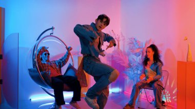 Çok kültürlü bir arkadaş kürsüde otururken Asyalı yetenekli bir dansçı modern müziğe geçiyor. Profesyonel dansçı, hipster takımı tezahürat yaparken ve desteklerken enerjik adımlar atıyor. Mutluluk.