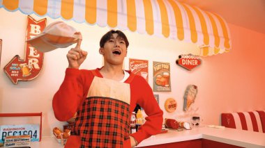 Profesyonel Asyalı restoran işçisi yemek hazırlar ve yemek barının arkasında durur. Kırmızı gömlekli ve kırmızı önlüklü mutlu garson kameraya bakarken serbest stil müziğe geçiyor. Çılgın dans. Mutluluk.