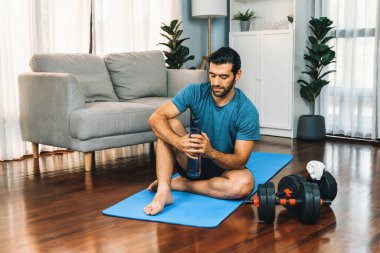 Atletik ve sporcu adam spor paspası üzerinde su içiyor. Vücut egzersizlerini bitirdikten sonra evdeki formda ve sağlıklı spor yaşam tarzı için egzersiz yapıyor. Gaiety evde egzersiz eğitimi.