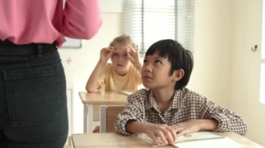 Asyalı ilkokul öğrencisi sınıfta öğretmenine bakıyor. Sınıfta oturan çeşitli zeki öğrenciler, öğretmenleri sınıf çalışmalarını ve sınavlarını anlatırken. Eğitim konsepti. Pedagoji.