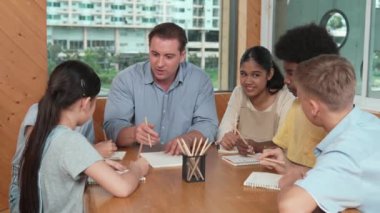 Çok kültürlü çocuklar resim çizerken ya da masa başında kalemle kağıt üzerinde not alırken zeki öğretmen konuşuyor ve işi anlatıyor. Otururken çeşitli öğrenci çizimleri ya da paylaşım fikirleriniz kutlu olsun. Öğretim