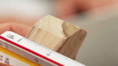 Yetenekli mimar ya da güvenlik mühendisinin video klibi, ev şeklindeki ahşap bloğu ölçmek için ölçü cetveli, ölçüm aracı kullanarak stüdyodaki bir masada ev inşaatı tasarlamak için kullanılıyor. Tanımlama.