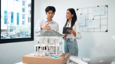 Güzel, genç, beyaz bir proje yöneticisi Asyalı mühendise, mühendislik masasında ev modelini ölçerken tablet kullanarak bina detaylarını anlattı. Tertemiz.