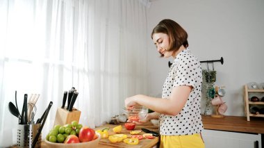 Kafkaseli anne kahvaltıda sebze pişirirken mutlu anne de modern mutfakta salata için taze malzemeler hazırlıyor. Hizmetçi sağlıklı yemek pişiriyor. Dikkat konsepti. Pedagoji.