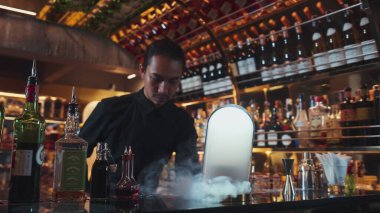 Asyalı barmen dumanlı klasik karışık viski kokteyli sunumu yapıyor. Harika bir sunum. İçecek tezgahı lüksünde özel, lezzetli, yaratıcı bir reklam içeceği öneriyor. Vinosity.