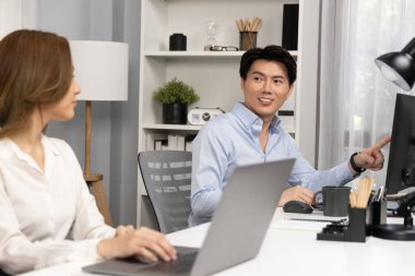 Gülümseyen Asyalı bir adam, yan görüntüdeki modern ofis çalışma masasında veri tabanını ararken günlük dizüstü bilgisayarla pazarlama raporu projesini planlarken kadın meslektaşıyla konuşuyor. İnfobahn.
