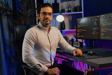 Bilgisayar ekranındaki yazılım geliştirme kodlamasına karşı poz vermek için akıllı bilişim geliştirici görünümlü kamera profilleri, neon ışıklı siber oda ofisinde program güncellemesi internet sitesi verileri sunuyor. Tahmin et..